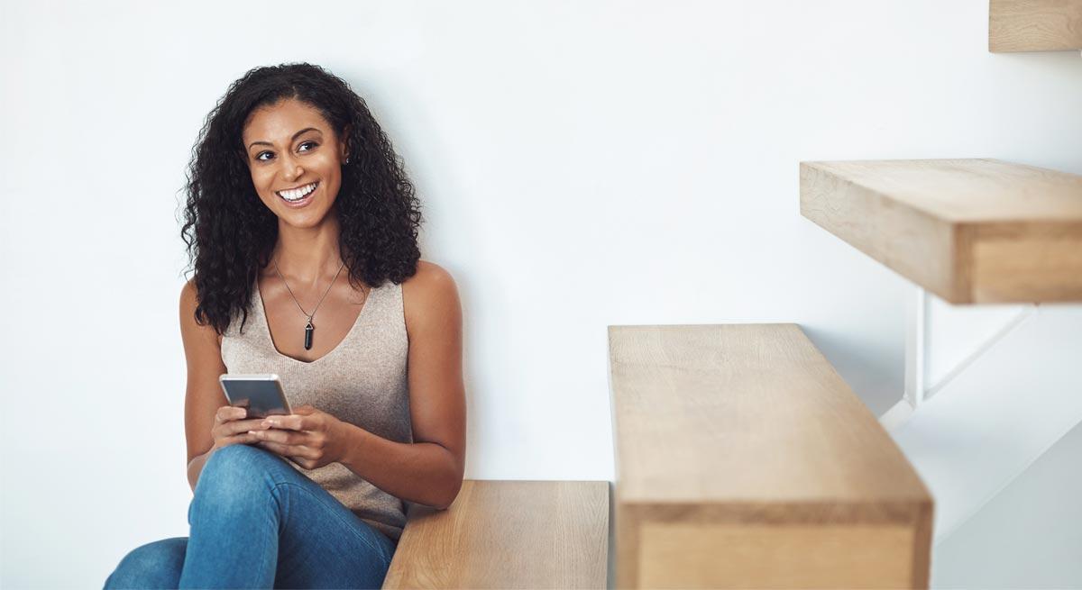 Photo of woman sitting inside looking at her mobile phone Photo of woman sitting inside looking at her mobile phone