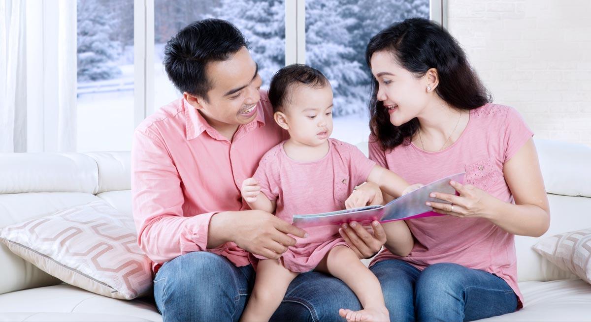 Photo of family with child sitting inside home reading a book in front of winter window Photo of family with child sitting inside home reading a book in front of winter window